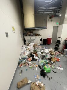 An overflowing trash dumpster and large pile of junk on the floor, indicating a need for junk removal service by Bay Area Bin Support in San Leandro, CA.