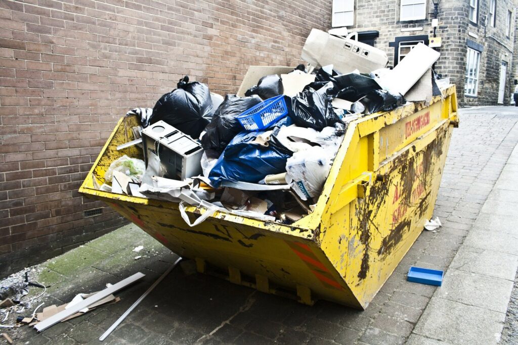 An overflowing yellow dumpster filled with household junk and trash on a street, ready for removal by Bee Green Recycling in Richmond, VA