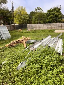 An overgrown yard with discarded metal sheets and wood planks, awaiting removal by SATX Junk-A-Haulics in San Antonio, TX.