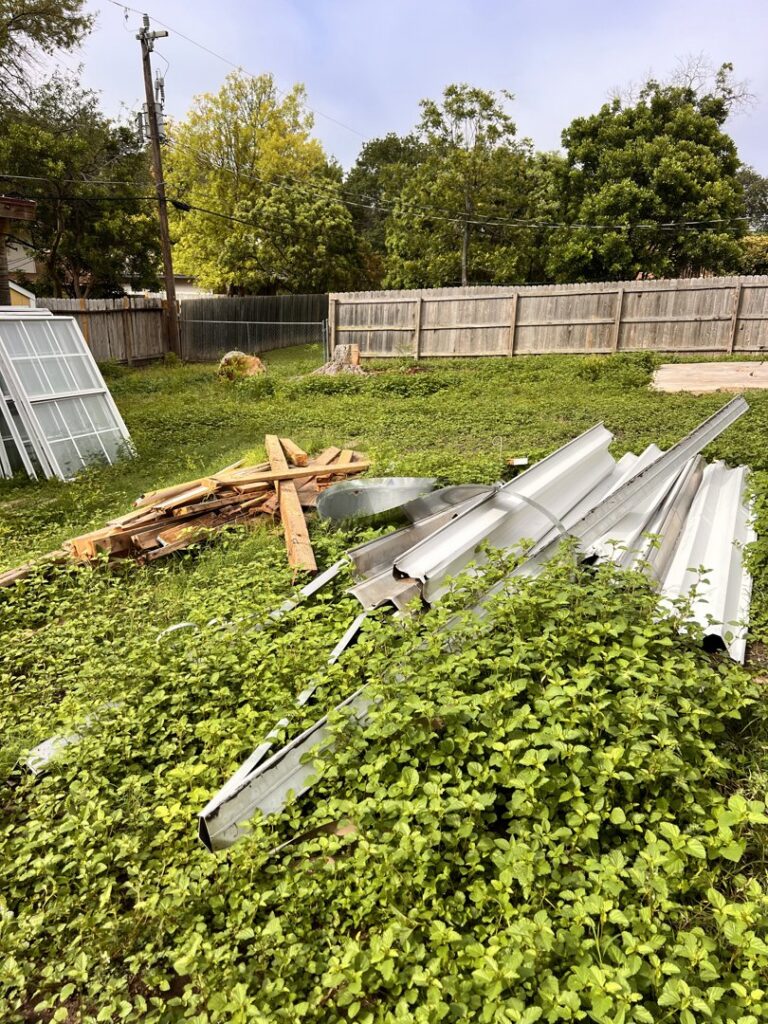 An overgrown yard with discarded metal sheets and wood planks, awaiting removal by SATX Junk-A-Haulics in San Antonio, TX.