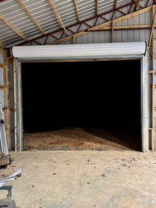 A newly installed overhead roll-up door partially open in a barn, showcasing services by AK Overhead Door & Handyman Services in Wetumpka, AL.