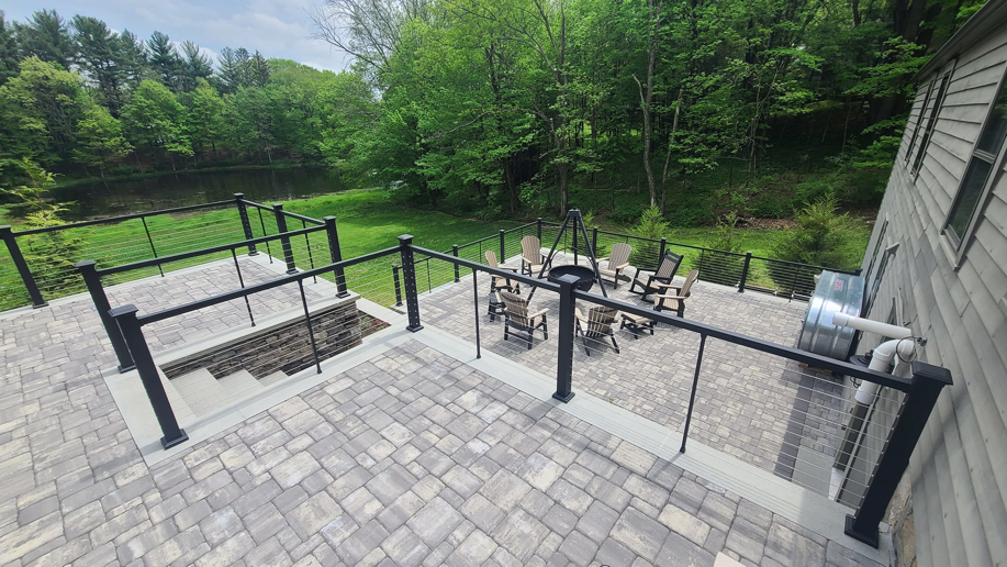An overhead view of a large paver patio featuring a built-in fire pit area and cable railings by David Hayden Construction LLC in Danbury, CT.