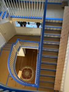Overhead view of a multi-story staircase with blue painter's tape on treads and balusters during renovation by S-G General Contracting LLC in Philadelphia, PA.