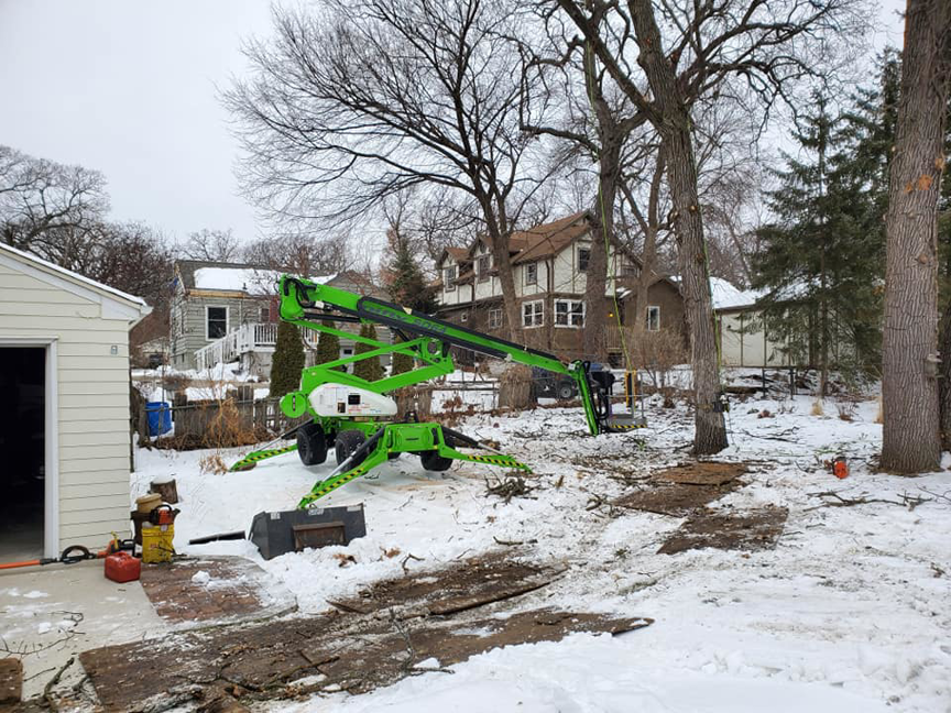 An overhead view of tree trimming work from an aerial lift, showing cut branches on the snowy ground by Beaver Tree Service in Des Moines, IA