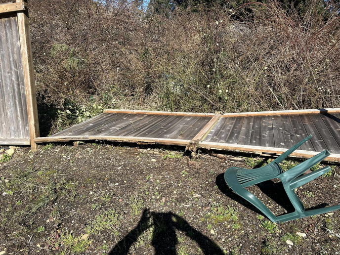 An overturned plastic chair next to a fallen wooden fence section, awaiting repair from HandyMan Shocks in Tacoma, WA.