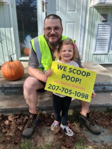 The owner and a child holding a 'We Scoop Poop!' sign for The Doo Doo Dudes in Lewiston, ME.
