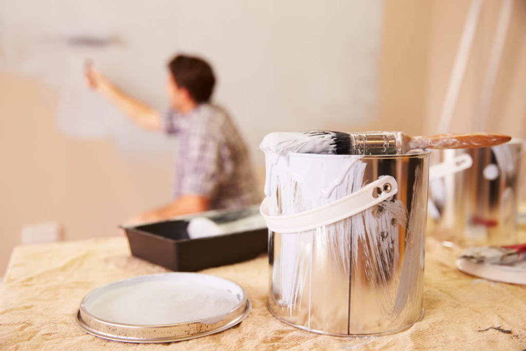 A close-up of a paint can and brush, with a painter working in the background for World General Construction LLC in Everett, WA.