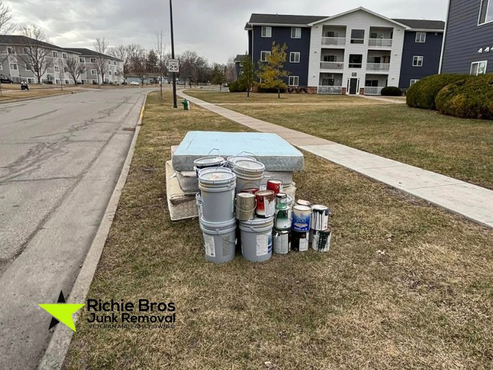 A stack of paint cans and a mattress placed on a grassy area for pickup by Richie Bros Junk Removal in Urbandale, IA.
