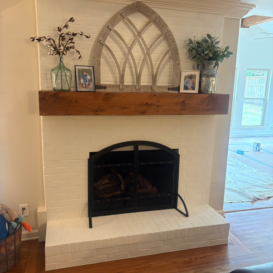 A newly painted white brick fireplace with a rustic wooden mantel installed by Archway Remodeling & Design LLC in Peachtree Corners, GA.
