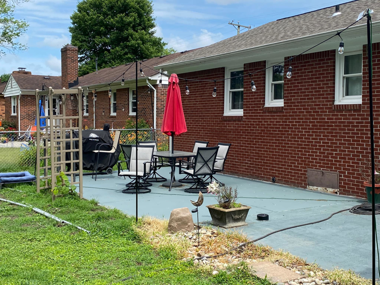 A finished painted concrete patio with an outdoor dining set and string lights by McGhee's Concrete in Chesapeake, VA.