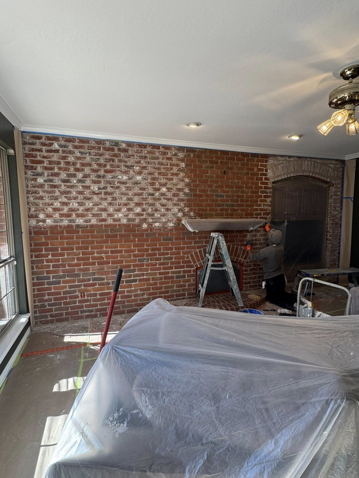 A painter whitewashing a brick fireplace wall, showing work in progress, by Pro Touch Painting Inc. in Oklahoma City, OK.