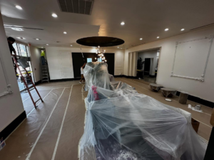 Painters on ladders working on an interior renovation project with covered furniture by Painting Services by David LLC in Houston, TX.