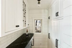 A narrow pantry or butler's pantry with white cabinets and a black countertop by Kornerstone Kitchens in Orlando, FL.