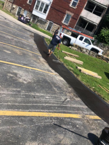 A handyman applying sealant to a parking lot, a service provided by Executive Property Construction at 301 Maple Blvd.