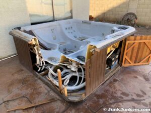 A partially dismantled hot tub on a patio, with exposed plumbing, ready for removal by Junk Junkees in Peoria, AZ.