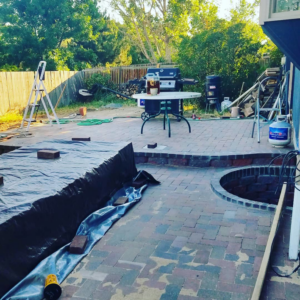 A patio area with a fire pit under construction, covered with a tarp, by Steveson Enterprises, Inc. in Golden, CO.