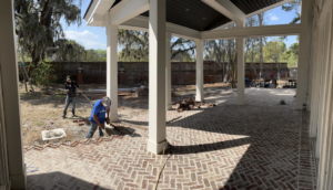 Two workers installing brick pavers on a patio, a handyman service by Half Moon Custom Homes in Rincon, GA.
