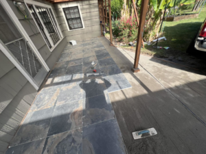 A handyman installing new patio tiles on an outdoor porch at a home in Portland, OR, by WorldWide Construction LLC.