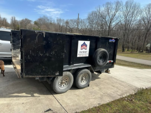A black dump trailer with the Patriot Dumpster Rental logo parked on a concrete driveway in Chattanooga, TN.