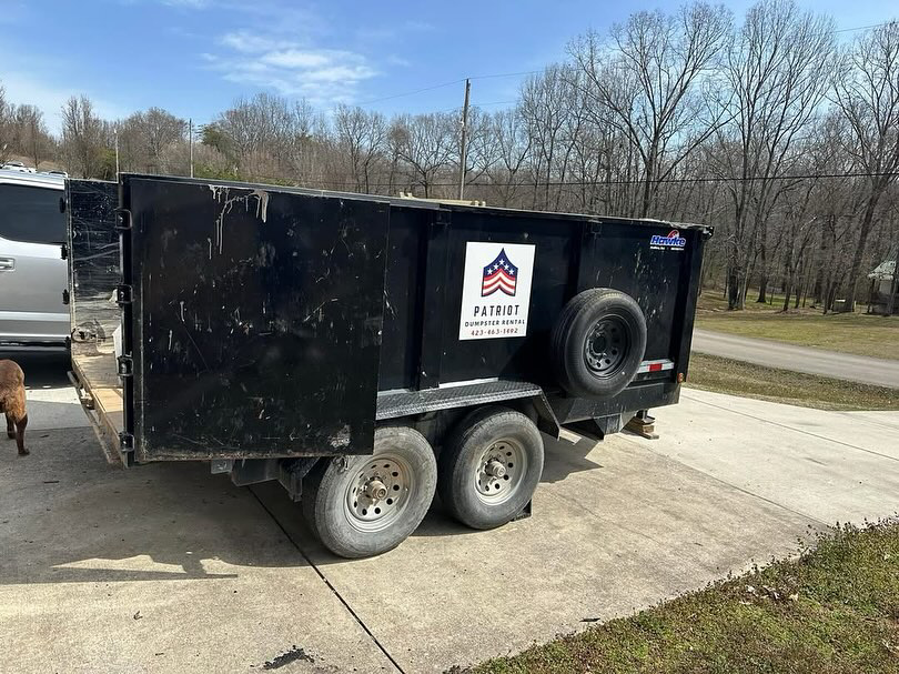 A black dump trailer with the Patriot Dumpster Rental logo parked on a concrete driveway in Chattanooga, TN.