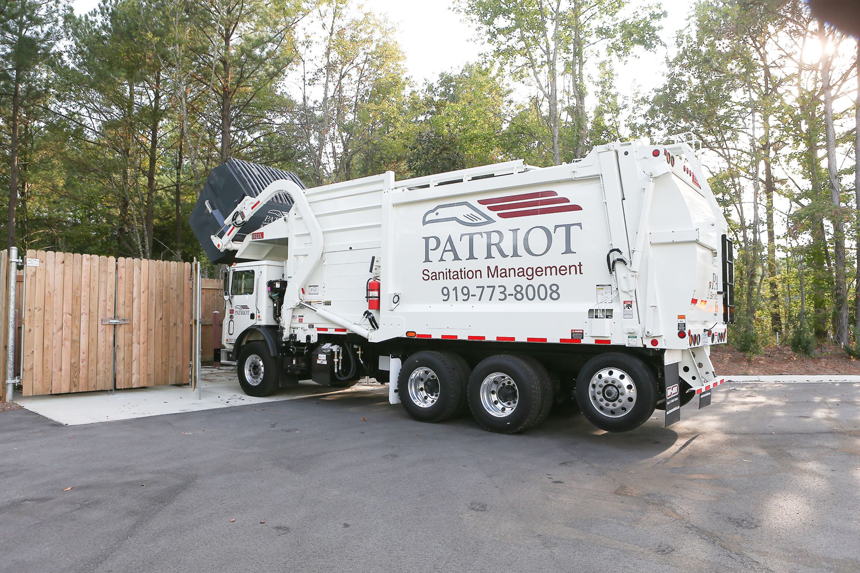 A Patriot Sanitation Management truck picking up a commercial dumpster for waste removal in Raleigh, NC