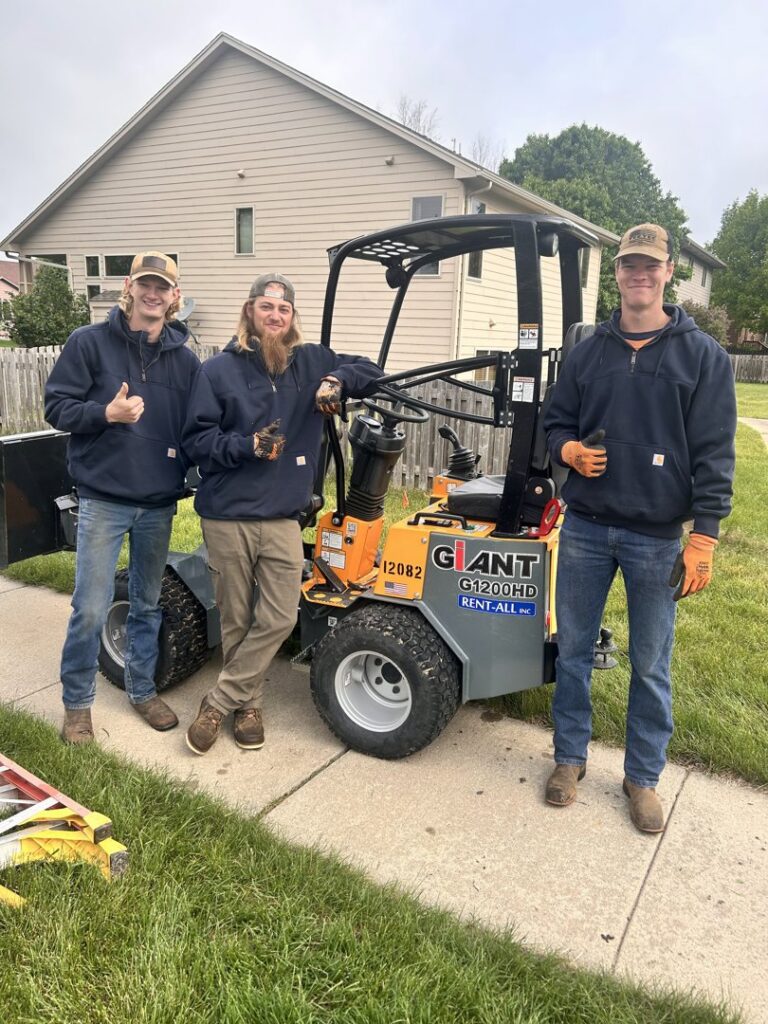 Three Patriot Tree Service crew members posing with a mini-loader on a job site in Sioux Falls, SD