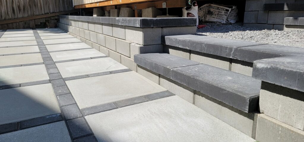 A close-up of a paved patio with steps and a retaining wall leading to a shed by LMS Landscapes & Fence services in Auburn, WA.