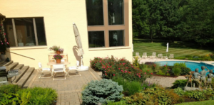A beautiful paved patio area next to a swimming pool with lush landscaping by Massa Paving Company in Cincinnati, OH.
