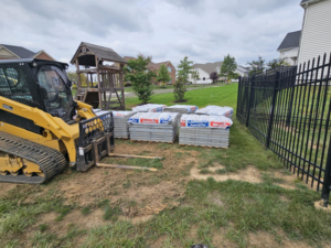 Pallets of pavers and a skid steer on a residential job site for Composite Pools USA in Newfield, NJ.