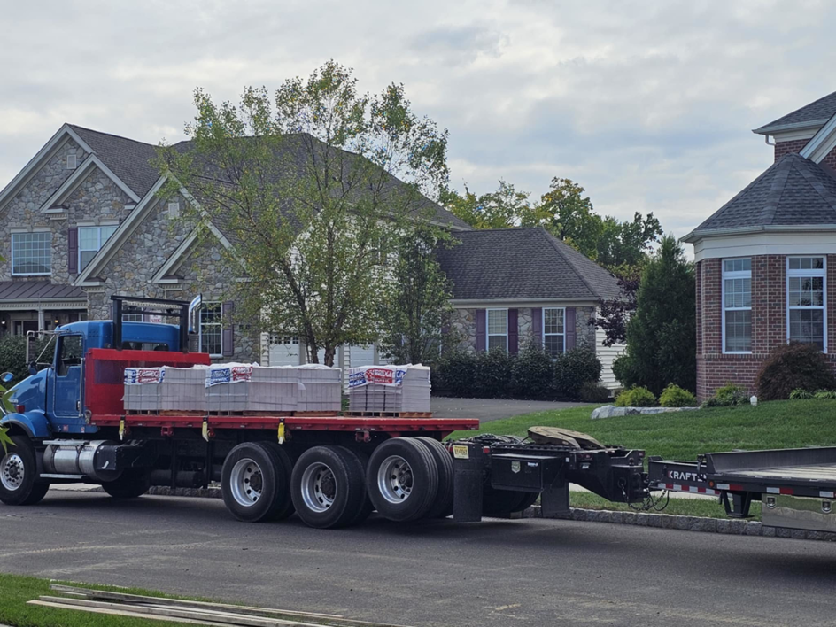 A flatbed truck delivering paver materials to a residential site for Composite Pools USA in Newfield, NJ.
