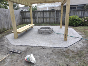 A newly installed paver patio with a fire pit and bench under a pergola by Signature Deck & Pergola in Virginia Beach, VA