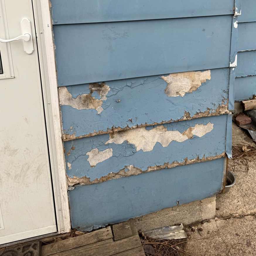 Peeling blue paint and damaged siding near a white door frame, indicating exterior repair work by Chris Pierce Construction in Sioux City, IA.
