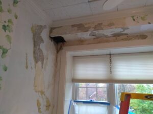 A wall with peeling wallpaper and damaged plaster, indicating a renovation or repair project by N. Bennecoff Drywall & Plaster in Lancaster, PA.