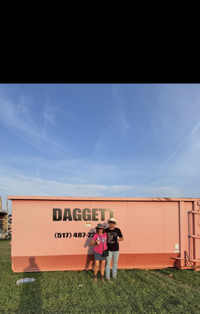 Two people standing with a pink Daggett Container Service LLC dumpster, ready for junk removal in Lansing, MI.