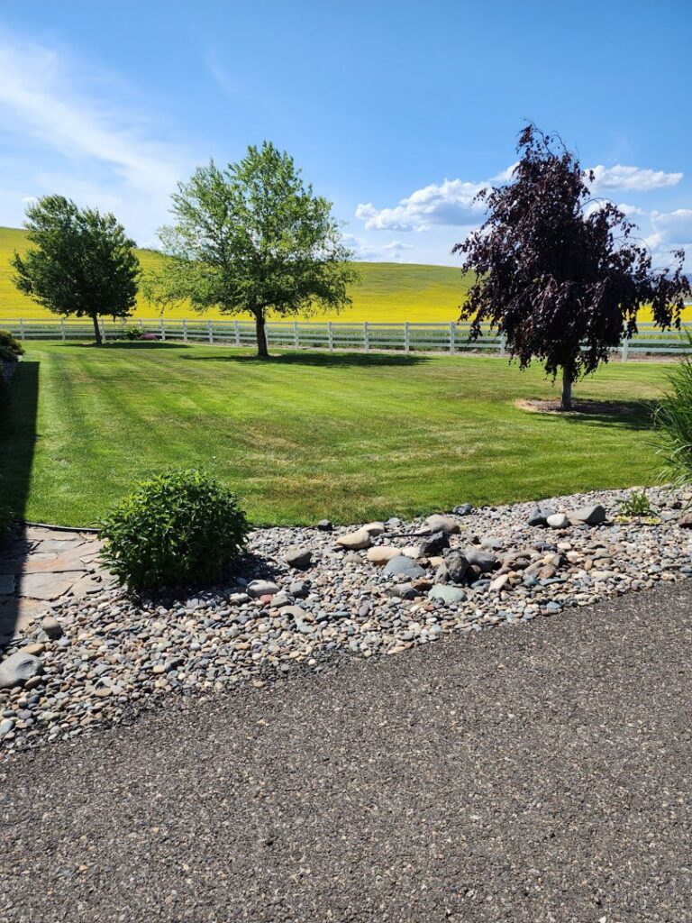 A perfectly mowed lawn with distinct stripes and a decorative rock bed, showcasing expert lawn care by Battleship Property Maintenance in Lewiston, ID.