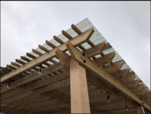 Close-up detail of a wooden pergola corner with a corrugated roof, showcasing craftsmanship by Fisher Construction, LLC in Selah, WA.