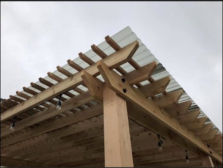 Close-up detail of a wooden pergola corner with a corrugated roof, showcasing craftsmanship by Fisher Construction, LLC in Selah, WA.