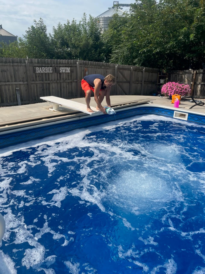 A person adding chemicals to a bubbly swimming pool as part of maintenance by Titan Handyman, LLC in Lewes, DE.