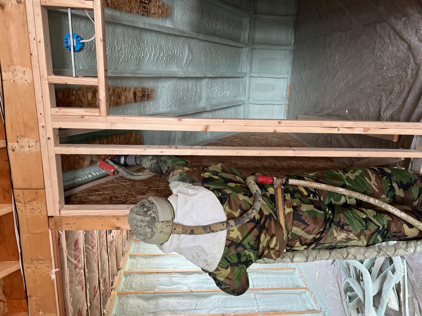 A person in protective gear applying spray foam insulation to walls in a new construction project by Insulation Man in Chesterfield, MI.