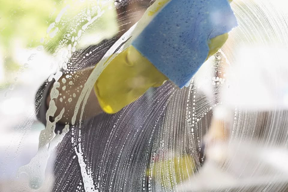 A person cleaning a window with a sponge, demonstrating window cleaning services by Gerald Jones Company in Durham, NC.
