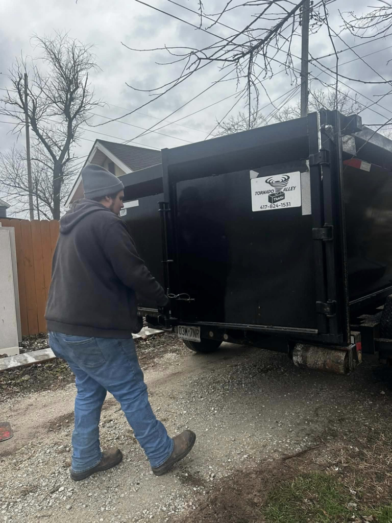 A person closing the back gate of a junk removal trailer for Tornado Alley Junk Removal & Trash in Springfield, MO.