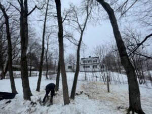A person cutting small trees or brush in a snowy, wooded area, demonstrating land clearing services by Russell Tree Works & Firewood Sales in Augusta, ME.
