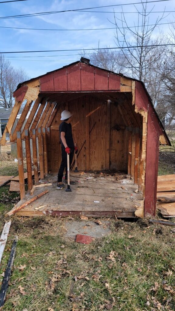 A person in a hard hat demolishing a shed, part of a junk removal service by T&G Dumping in Lorain, OH.