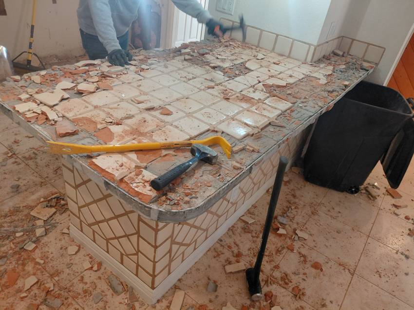 A person actively demolishing a tiled counter with tools, part of a demolition service by Arizona Junk Removal LLC in Phoenix, AZ
