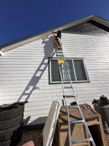 A person on a ladder installing exterior lights on a house, a service by Ambition Services Llc in Greeley, CO.