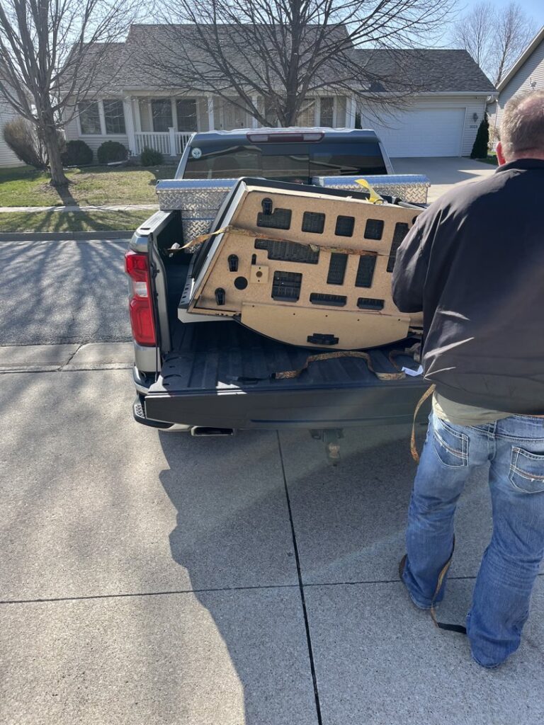 A person loading a large, bulky wooden item into the back of a pickup truck for Load and Go Junk Removal in Ames, IA.