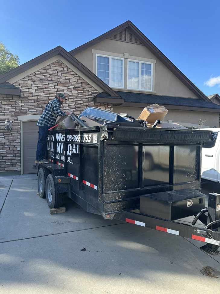 A person loading various junk items into a dump trailer for Haul My Load LLC in Caldwell, ID.