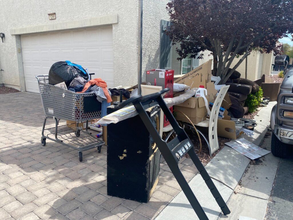 A person wearing gloves loads a bag of trash into a large blue dumpster, demonstrating junk removal by Mike's Dumper in Las Vegas, NV.