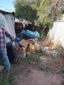 A person standing next to a large pile of household junk and debris in a yard, ready for removal by Vista Clean Junk Removal in Tucson, AZ.