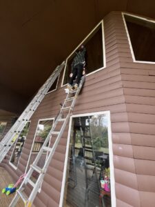 A person on a ladder performing exterior work near a window on a house, a service offered by OG Renovations in Huntington, WV.